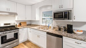 A modern kitchen with white cabinets, stainless steel appliances, a granite countertop, and a window providing natural light. - Gainesville Getaway - Spacious, Fire Pit & Yard! (Gainesville)