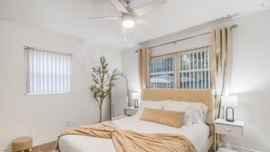 A bedroom with a bed, bedside tables, a nightstand, a ceiling fan, a window with blinds, and a plant. - Gainesville Getaway - Spacious, Fire Pit & Yard! (Gainesville)
