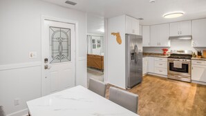 A modern kitchen with white cabinetry, stainless steel appliances, and a dining area with a marble table. - Gainesville Getaway - Spacious, Fire Pit & Yard! (Gainesville)
