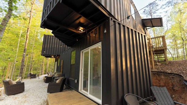 Uma cabana moderna com varanda, área de estar externa e uma grande porta de vidro deslizante.