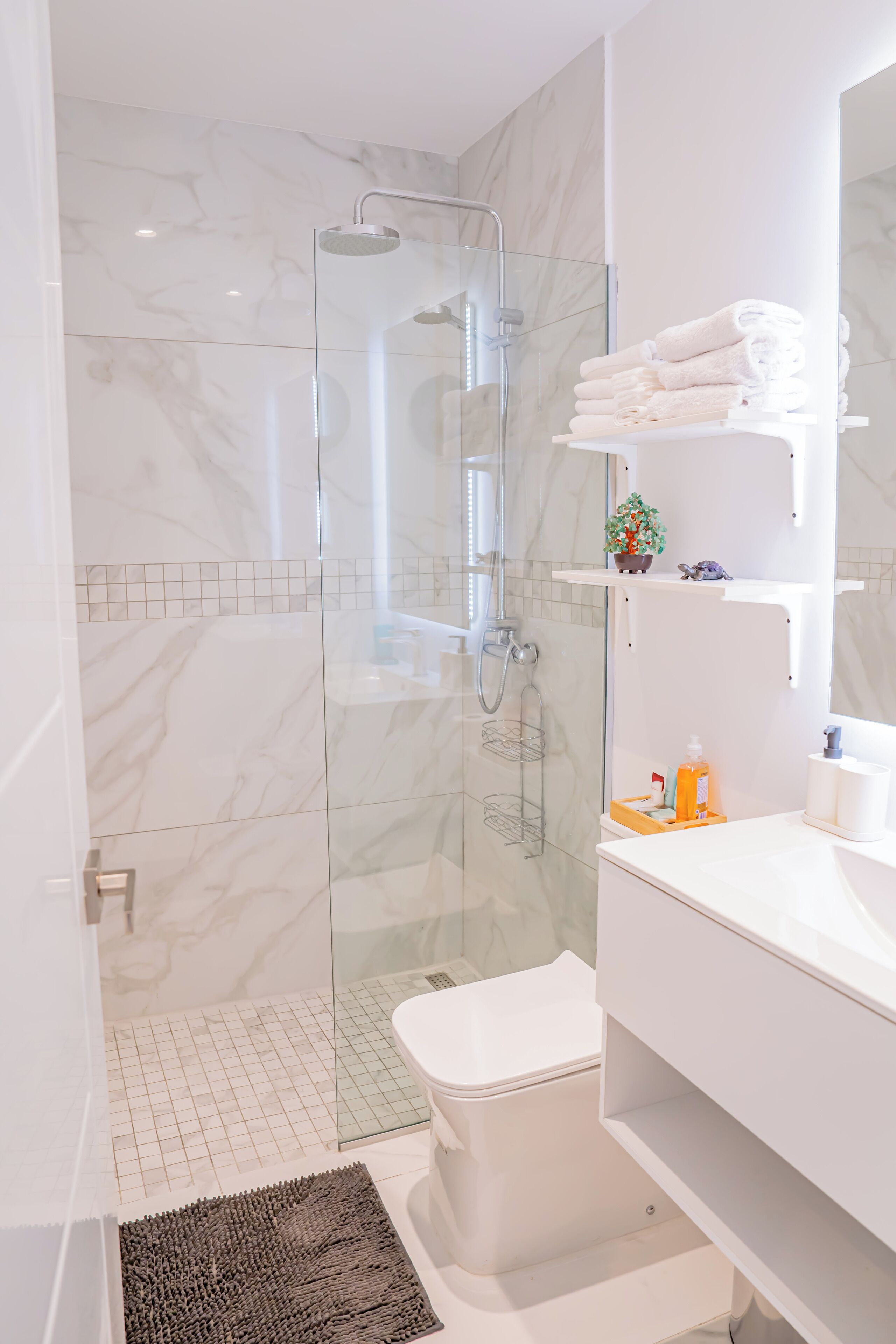 A modern bathroom with a glass-enclosed shower, a white toilet, and a sink with a towel rack.