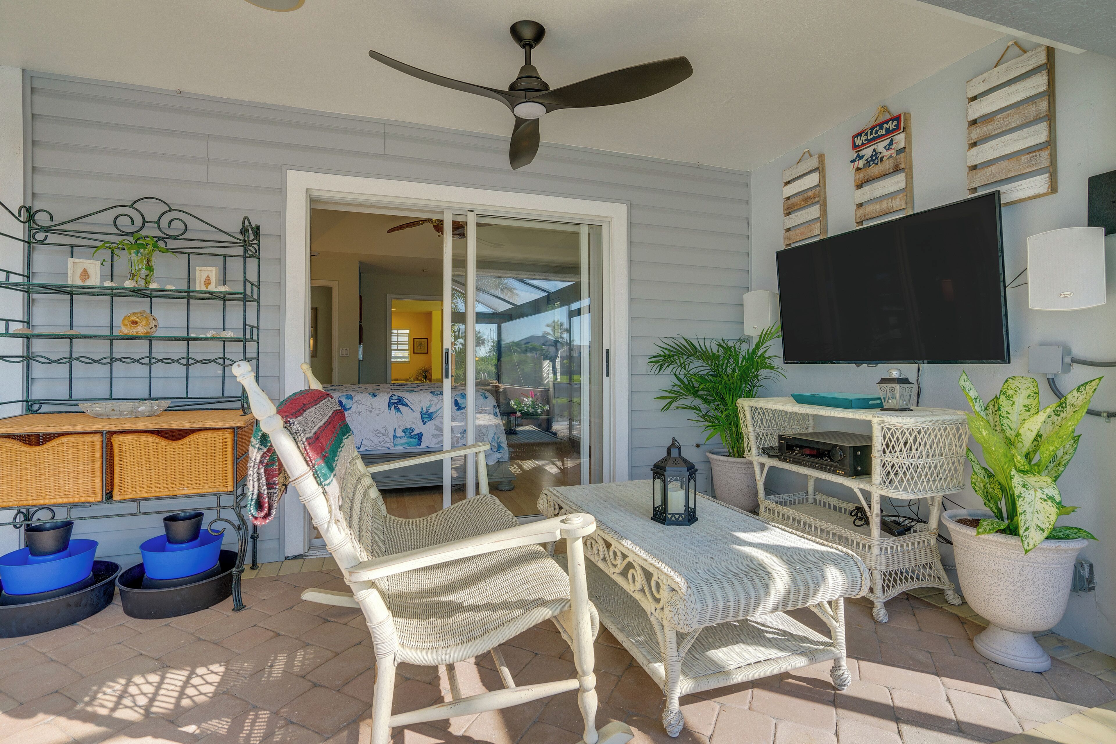 A patio area with wicker furniture, a ceiling fan, a TV, and potted plants.