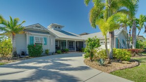 A two-story house with a covered porch, a driveway, and surrounding palm trees.