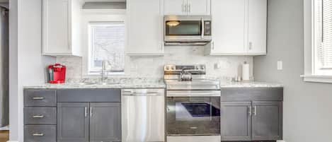 Una cocina moderna con armarios blancos, lavavajillas de acero inoxidable, horno empotrado y microondas.