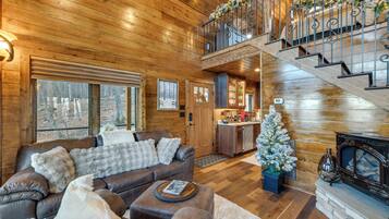 L’intérieur chaleureux d’un chalet, avec un revêtement mural en bois, une cheminée, un escalier et un petit coin cuisine.