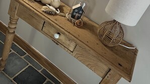 Ett konsolbord i trä med dekorativa föremål, inklusive keramiska kaniner, en glaskonstprydnad formad som ett hus, en flätad korg och en lampa.