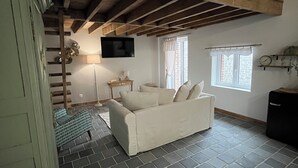 Ett vardagsrum med en soffa, en tv som är monterad på väggen, ett fönster med gardiner och en trappa som leder upp till en övre våning.