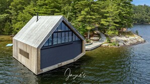 Uma cabana de madeira com telhado triangular em um lago cercado por árvores.