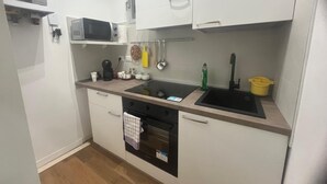 Et lille køkken med hvide skabe, en mikroovn, en komfur og en vask.