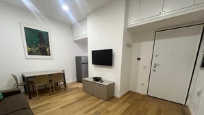 En moderne stue med spiseplads, et fladskærms-tv på væggen, et gråt skab og en dør med håndtag.