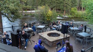 An outdoor deck with tables and chairs, a stone fire pit, and a river view. - River & Ranch Retreat: Fish, Raft, Hike & Ride in Rocky Mountain Bliss (Almont)
