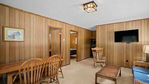 A room with wooden panel walls, a dining table with chairs, a television mounted on the wall, and a small table with a lamp. - River & Ranch Retreat: Fish, Raft, Hike & Ride in Rocky Mountain Bliss (Almont)