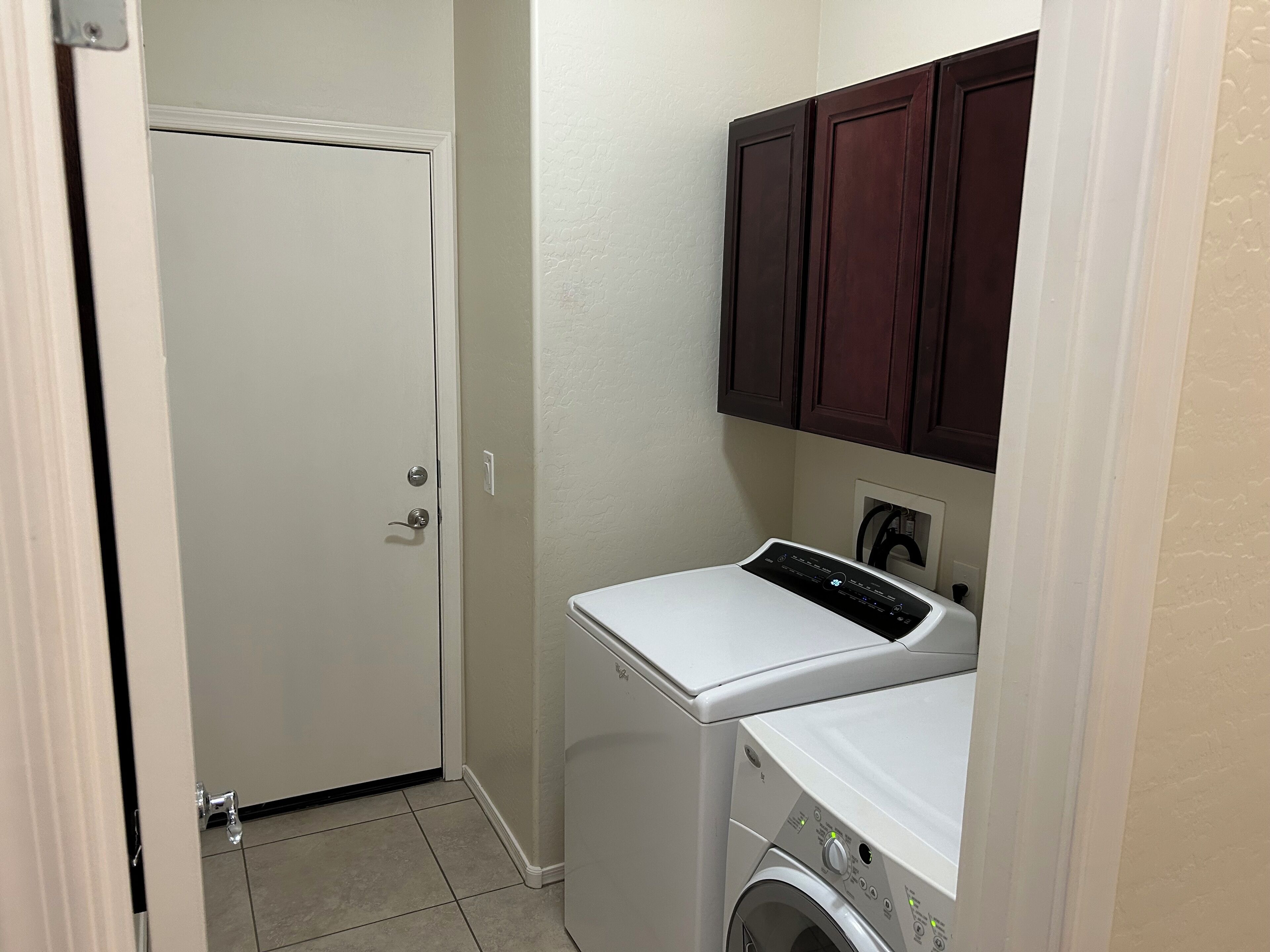 A compact laundry room with a washing machine and dryer, a door, and wooden cabinets above.