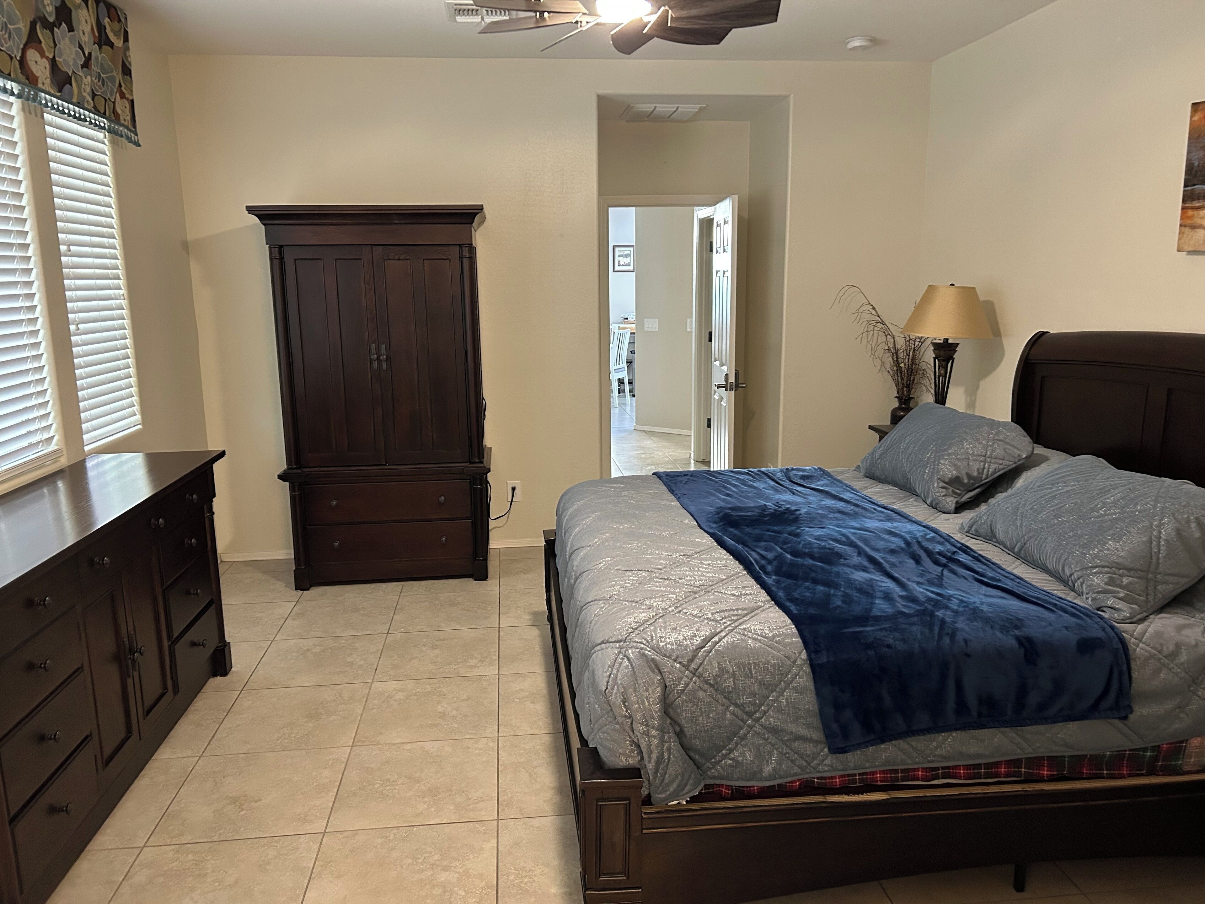 A bedroom with a bed, dresser, wardrobe, and a ceiling fan.