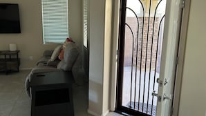 Ein Wohnzimmer mit einer Couch, einem Fernseher und einer Glasschiebetür, die zu einer Außenpatio führt.