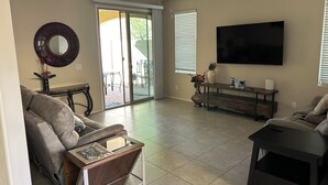 Ein Wohnzimmer mit Sofa, Couchtisch, Fernseher und einer Schiebetür zu einer Terrasse.