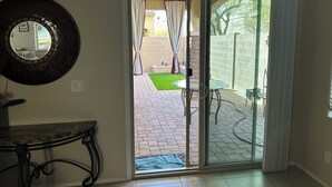 Ein Zimmer mit einer Schiebeglastür, die auf eine Außenpatio mit Pflasterboden, einem kleinen Tisch und einem Stuhl führt.