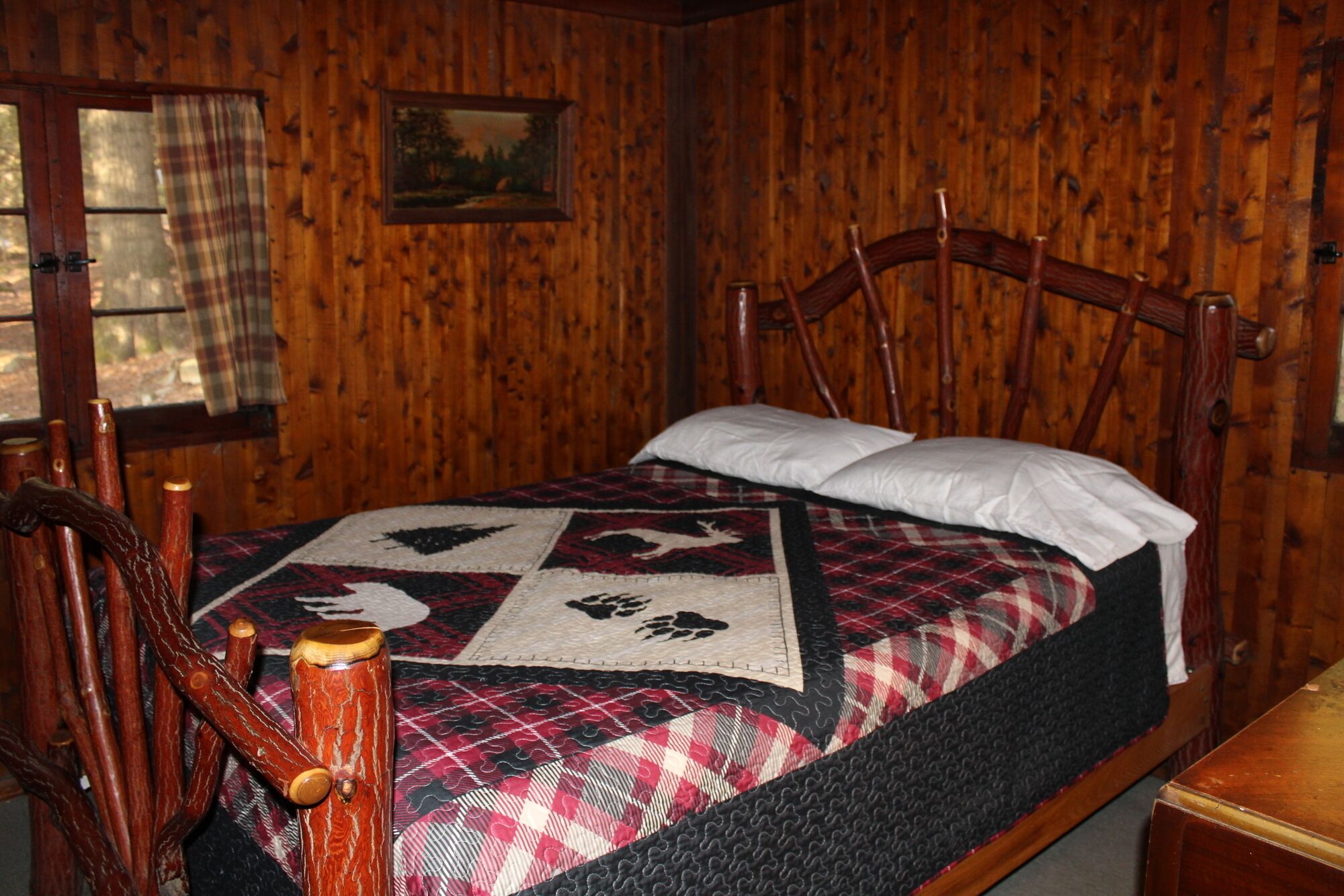 Una habitació de fusta amb un llit, una cadira i una finestra amb cortines.