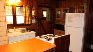 Een keuken met houten kasten, een witte koelkast, een gasfornuis en een spoelbak.