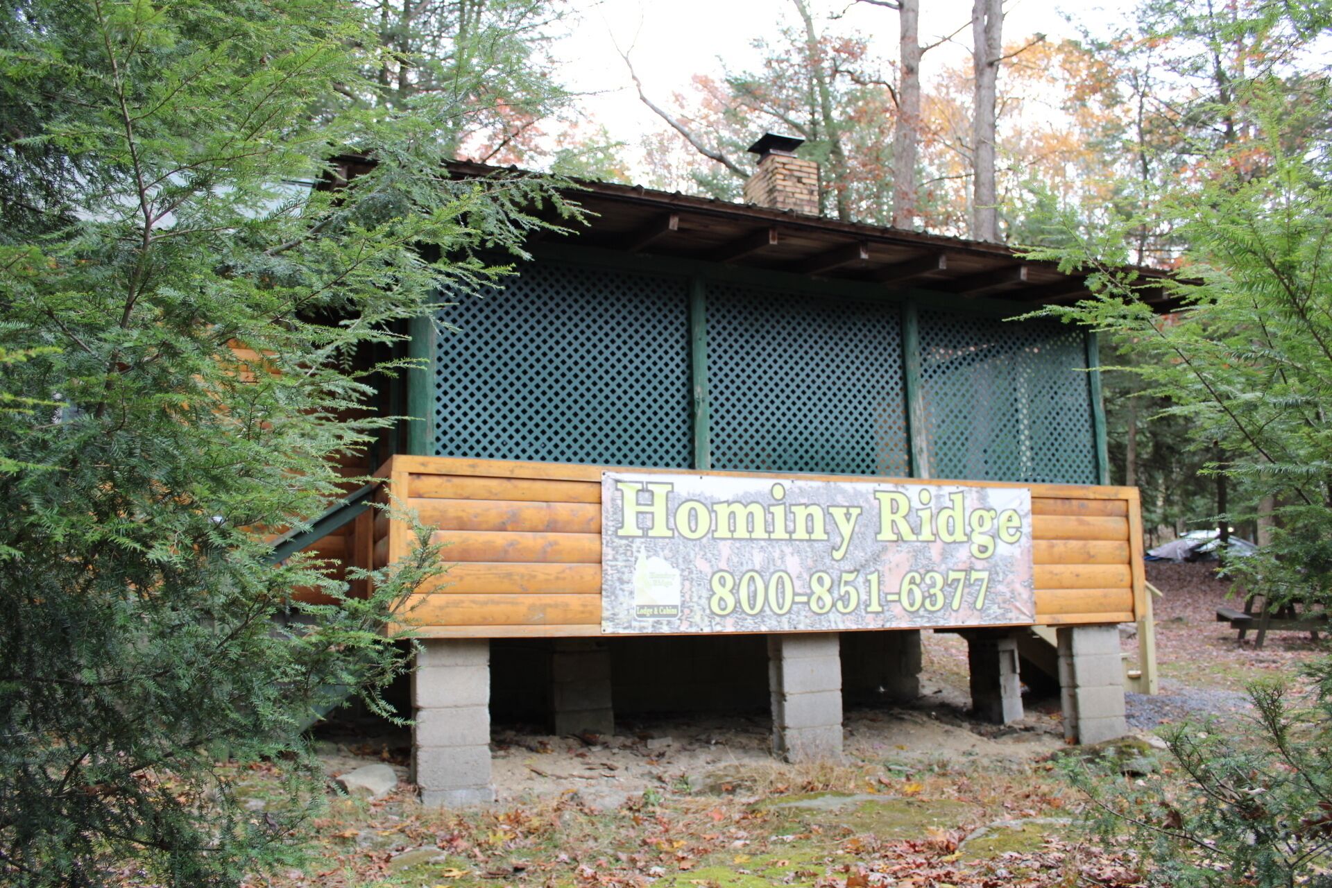 Una cabaña de madera con un letrero que muestra el nombre 'Hominy Ridge' y un número de teléfono.