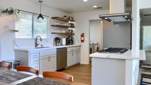 Een moderne keuken met witte kastjes, een ingebouwde kookplaat en een raam met jaloezieën.