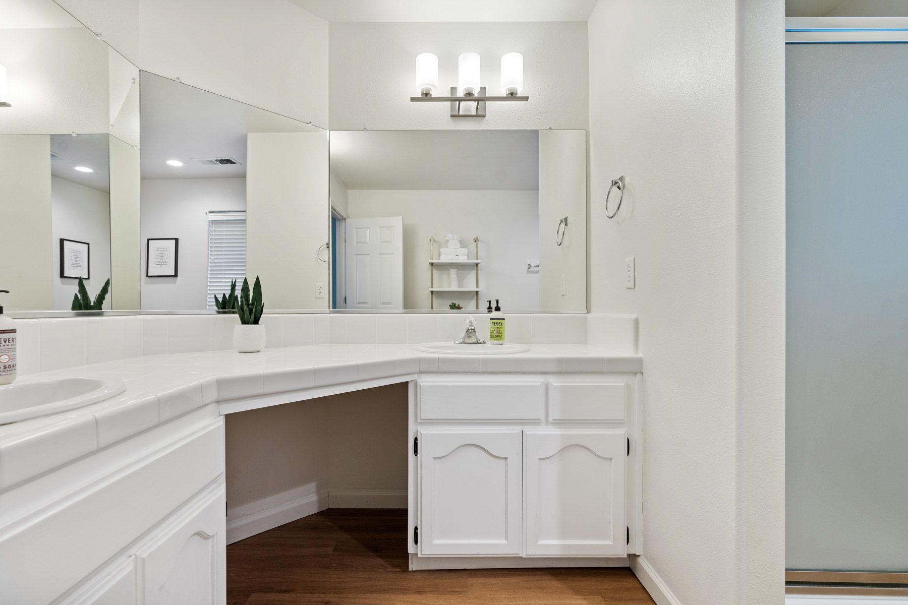A modern bathroom with a large mirror, white cabinetry, and a wooden floor.
