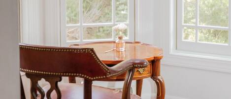 A room with a wooden chair and a table by a window with white blinds.