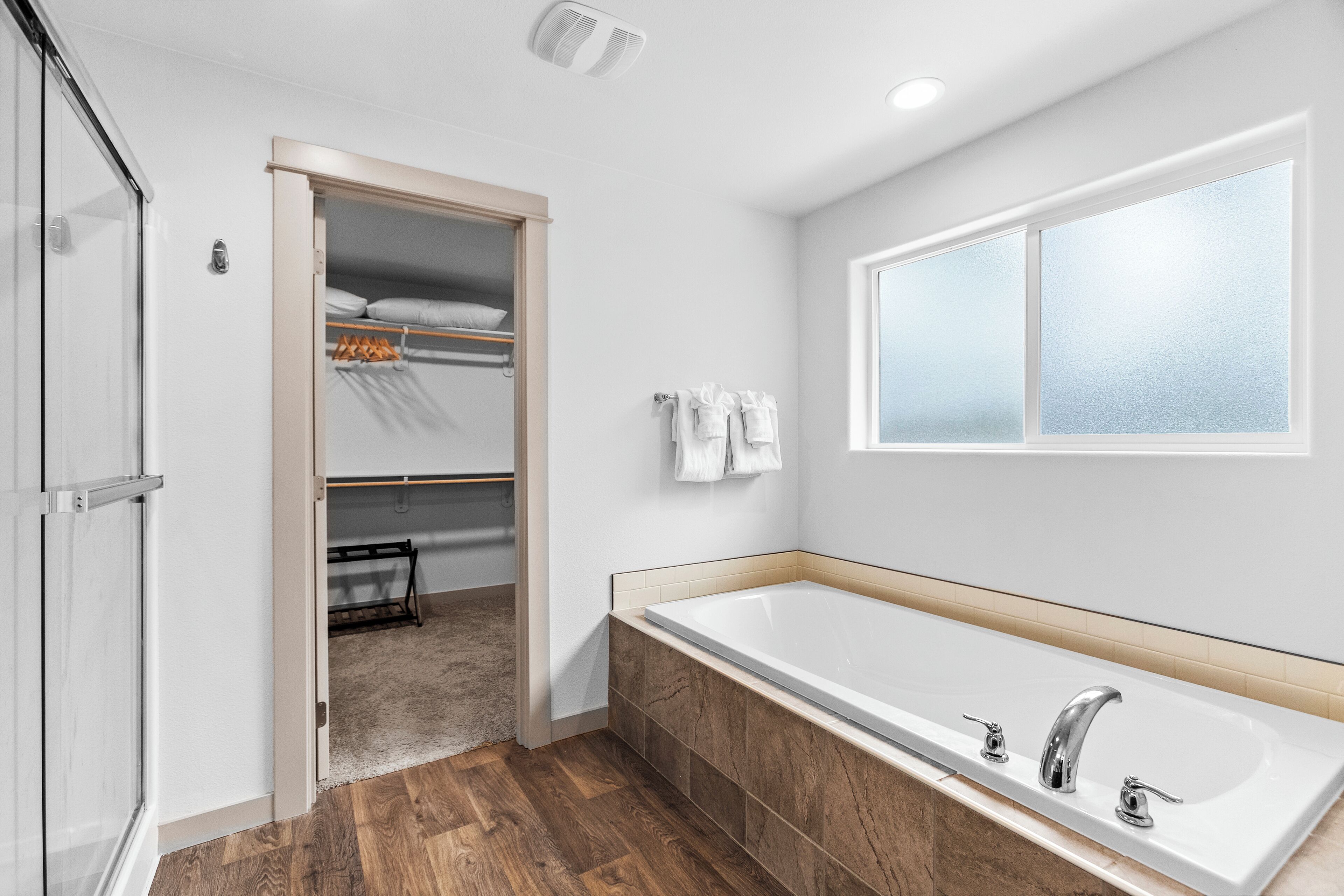 Un baño moderno con una bañera grande, piso de madera y un vestidor con ropa colgada.