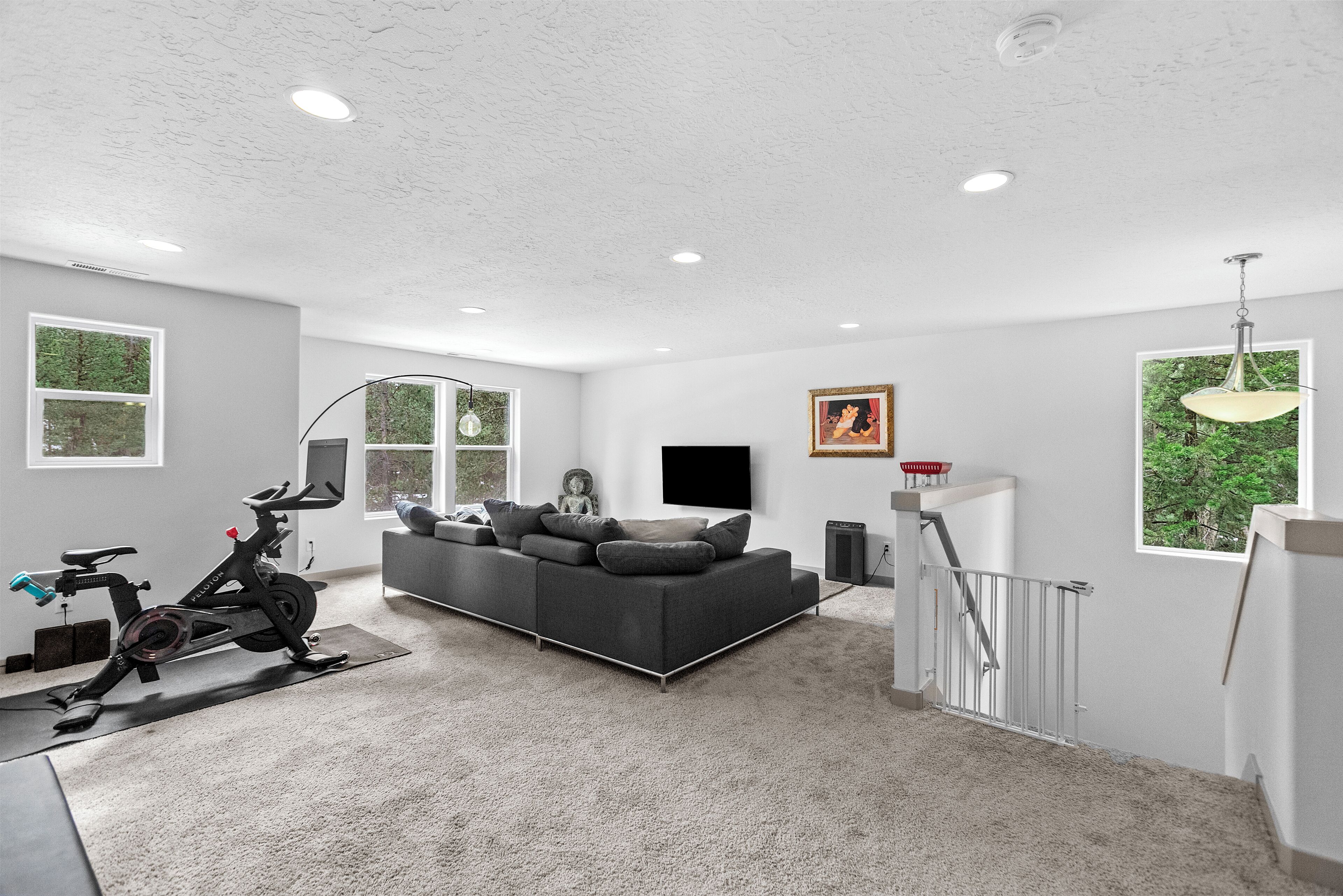 A spacious living area with a gray sofa, a standing exercise bike, and a staircase leading to an upper level.
