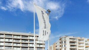 Een vlag met de tekst 'Blankenberge' op een vlaggenmast voor een helderblauwe lucht.