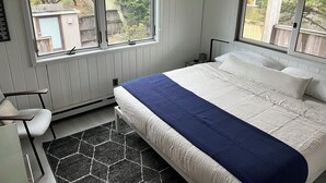 A bedroom with a bed, two windows, a chair, a heater, and a view of the outside. - Fire Island Pines Oasis w/4 King Bdrms, Heated Pool, Hot Tub, Ocean & Bay Views (Sayville)