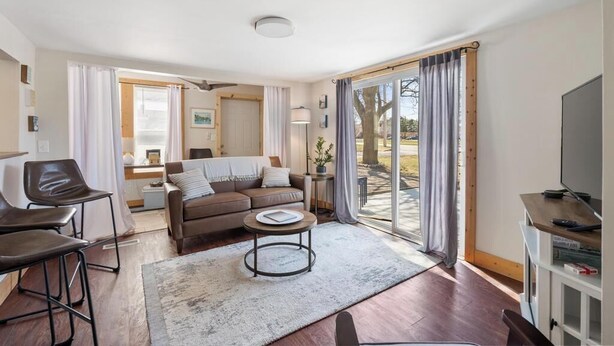 A modern living room with a sofa, coffee table, and chairs, a television, and a large sliding glass door to the outdoors.