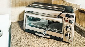 A kitchen with a built-in cabinet containing white dishes, glasses, and a toaster oven.