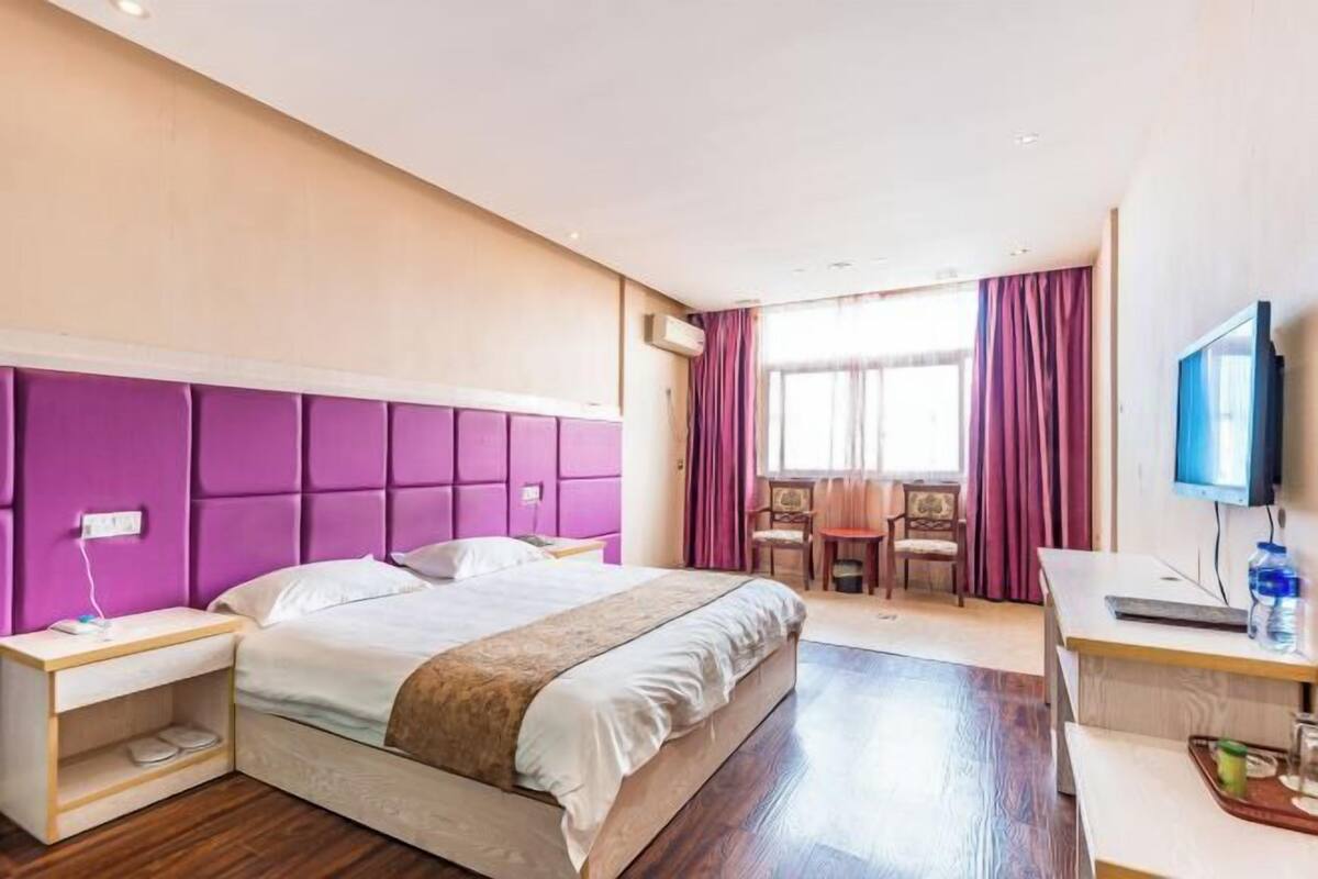 A hotel room with a bed, a desk, a chair, a TV, and a window with curtains.
