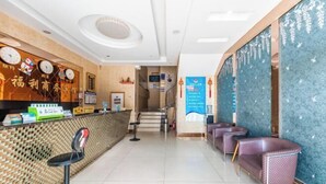 A hotel reception area with a reception desk, a waiting area with chairs, and a staircase leading to the upper floors.