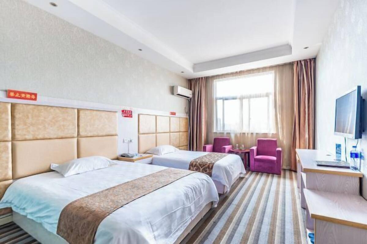 A hotel room with two beds, a desk, a chair, and a television.