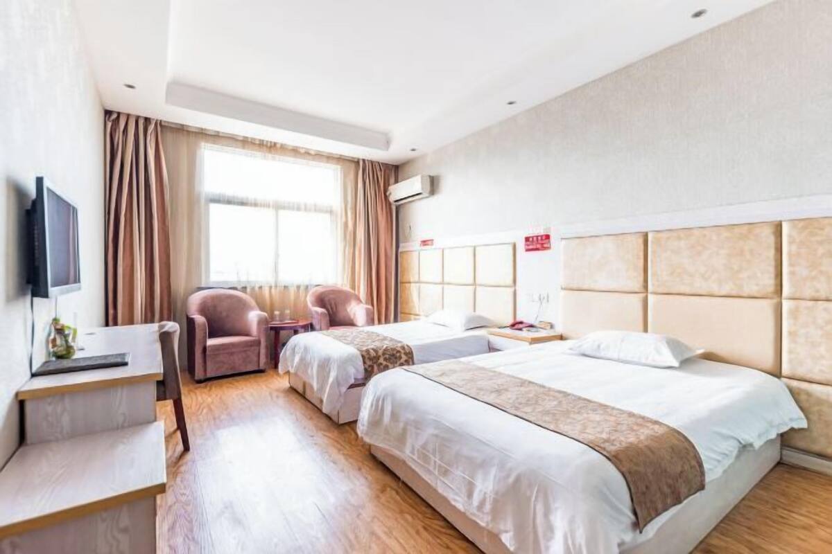 A hotel room with two beds, a desk, a chair, a TV, and a window with curtains.