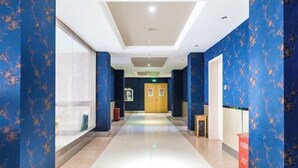 A hotel corridor with blue patterned walls, a tiled floor, and a central door with signage.