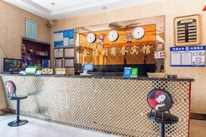 Un comptoir d’accueil d’hôtel avec une horloge, un ordinateur et un espace salon.