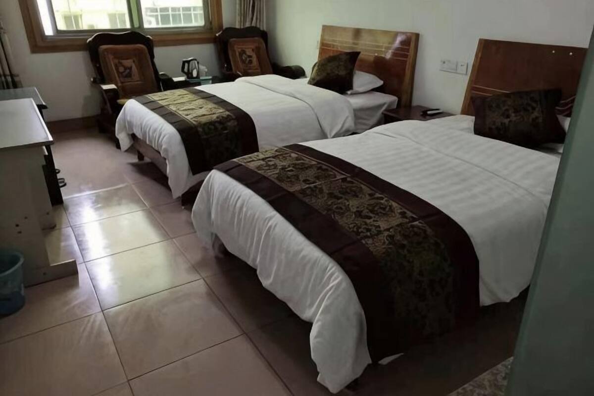 A hotel room with two beds, a desk, a chair, and a window.