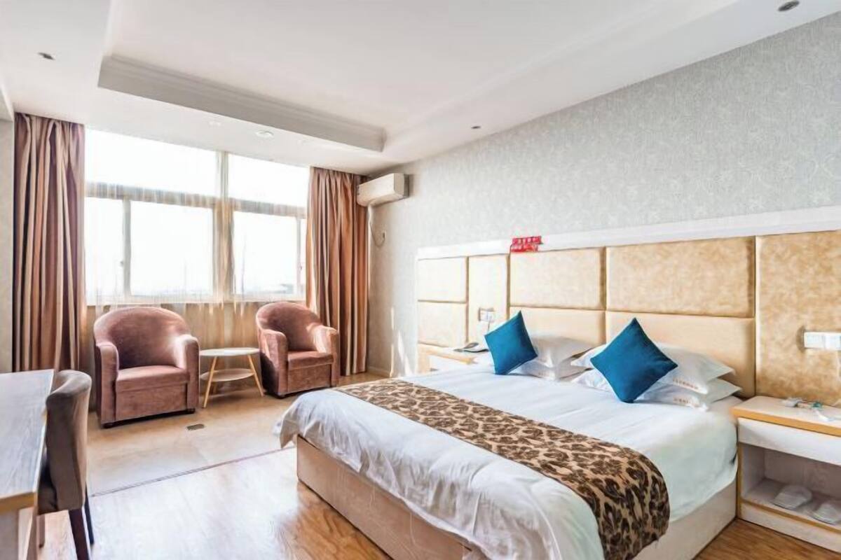 A hotel room with a bed, two armchairs, a table, and a nightstand.