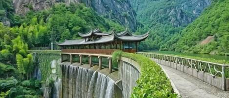 A traditional building with a curved roof, situated beside a waterfall and a river, surrounded by lush greenery and mountains.