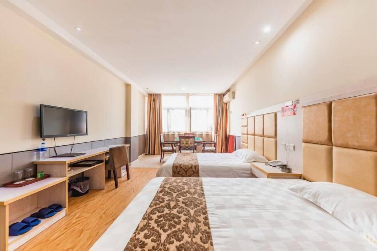 A hotel room with two beds, a desk with a computer, a TV, and a view of the outside.