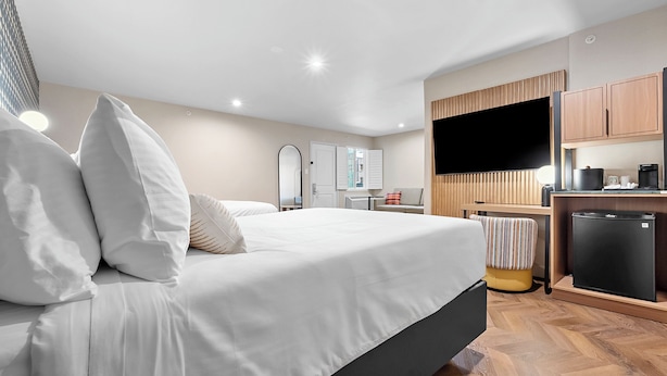 Una habitación de hotel moderna con una cama grande, un televisor de pantalla plana, una pequeña cocina y un espejo.