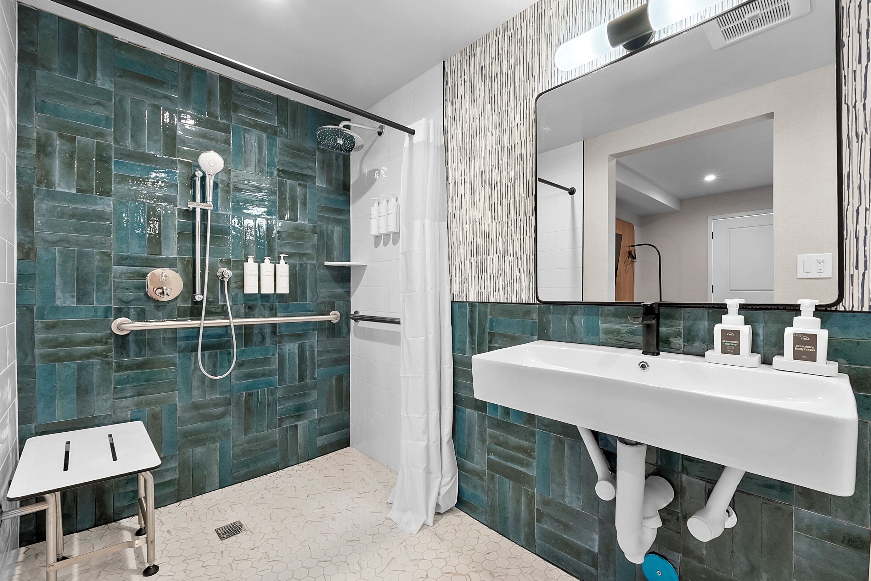 A modern bathroom with a glass shower enclosure, a white sink with soap dispensers, and a small white table.