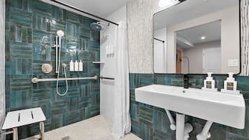 A modern bathroom with a glass shower enclosure, a white sink with soap dispensers, and a small white table.