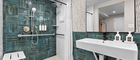 A modern bathroom with a glass shower enclosure, a white sink with soap dispensers, and a small white table.