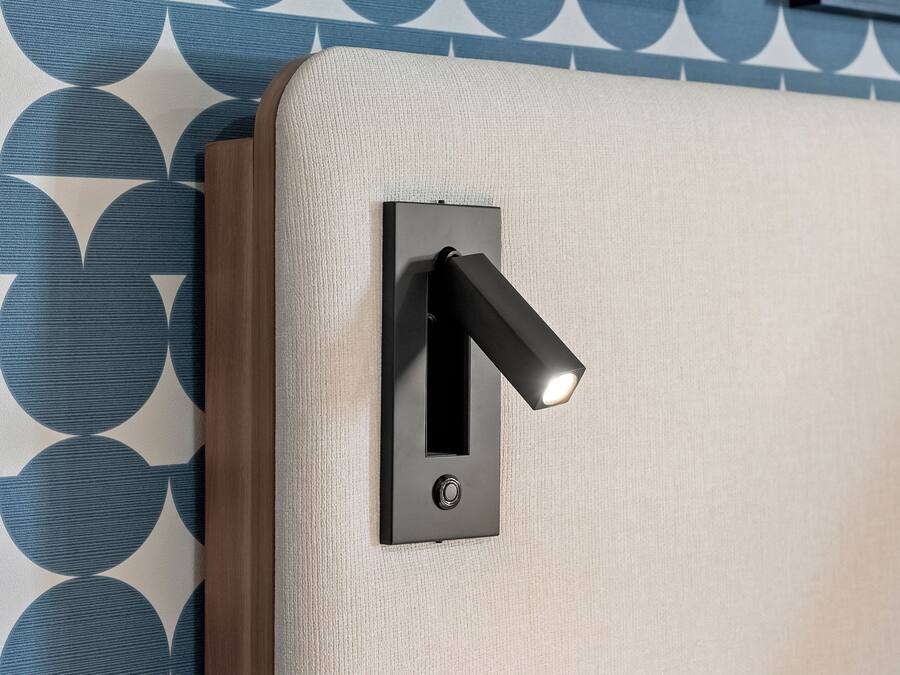 Un luminaire mural fixé au mur, doté d’un interrupteur à tirette, placé sur un mur texturé orné d’un motif géométrique.