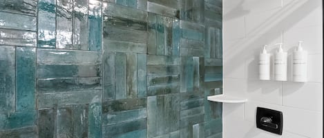 A bathroom with a herringbone tile pattern in shades of blue and gray, a black showerhead, and a white shelf with three bottles of Bosquet body wash.