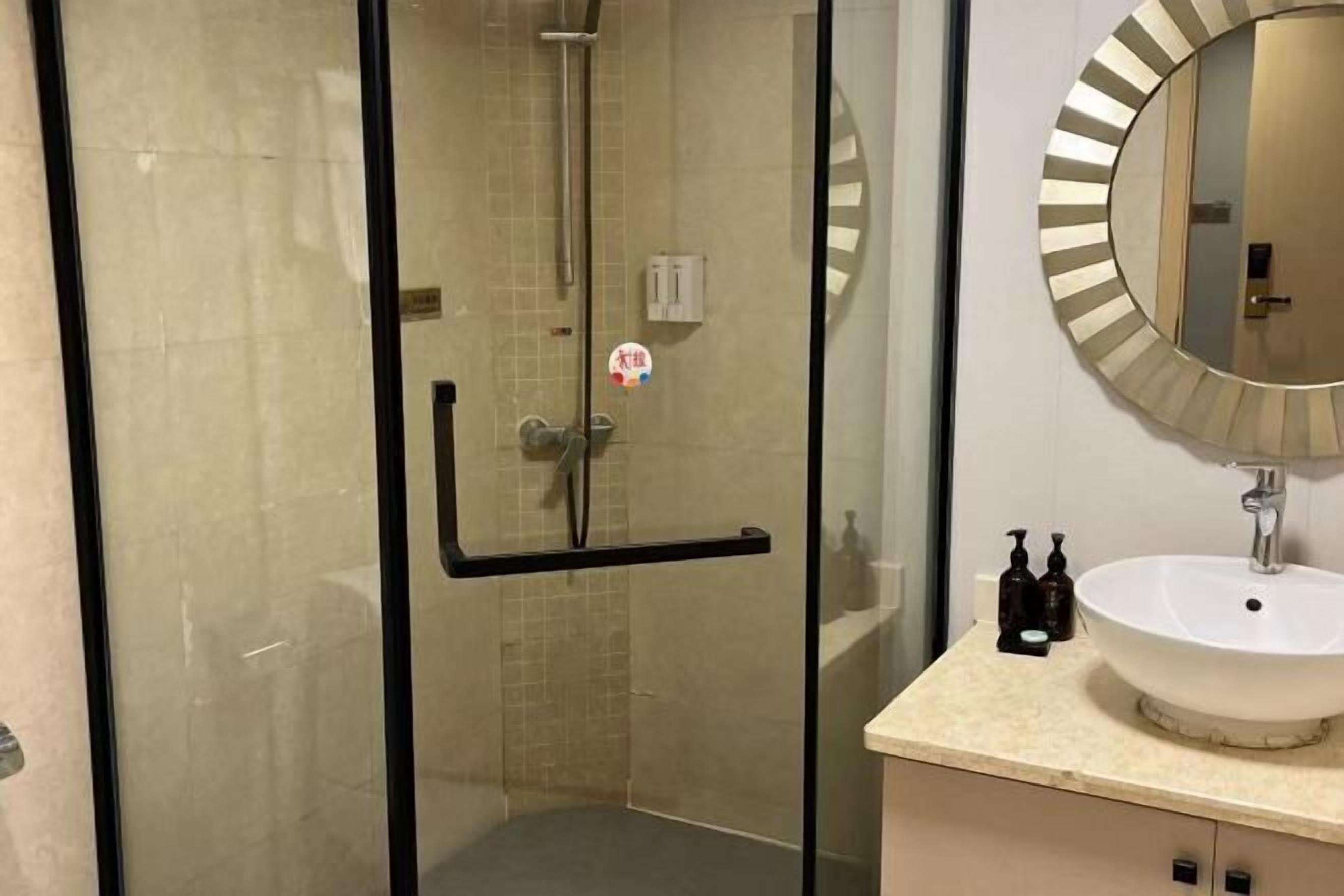 A modern bathroom with a glass-enclosed shower, a round mirror, and a white sink with a beige countertop.